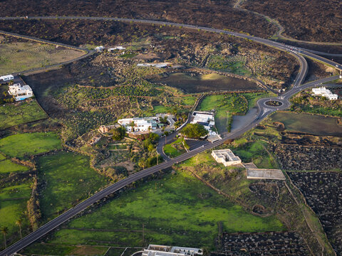 Aerial view of vibrant green fields meet volcanic rock formations, creating a striking contrast near winding roads and buildings, Lanzarote, Canarias, Spain.