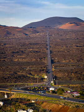 Aerial view of a seemingly endless road cutting through the volcanic landscape towards a distant mountain peak, Lanzarote, Canarias, Spain.