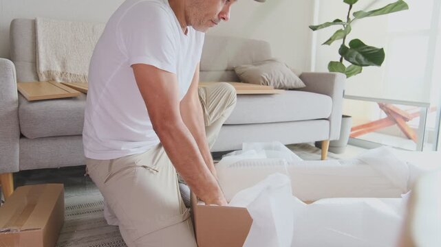 Focused man carefully unpacking and putting together a new piece of furniture in his living room