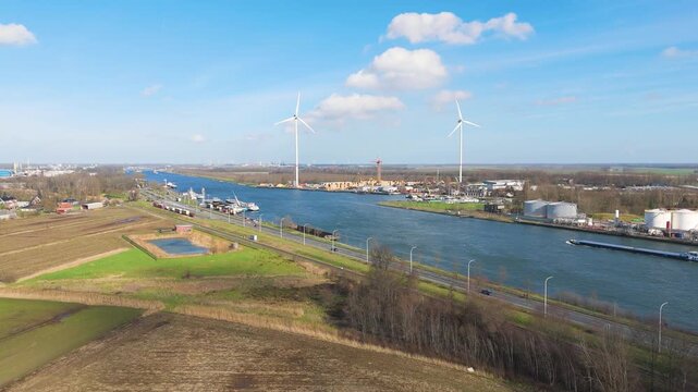 blue waterway threads through farmland infrastructure port facilities wind turbines extend horizon along canal zelzate toward shipping channel industrial complex agricultural land 