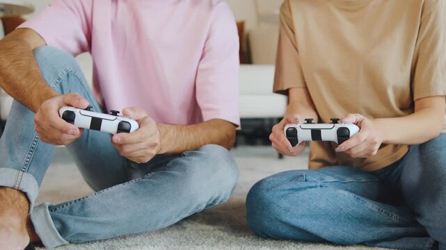 Close up hands of two people play video games on the floor in a living room together during an indoor game session