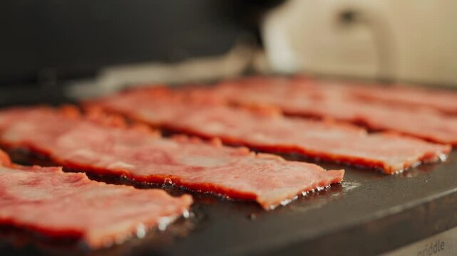Slices of turkey bacon cooking on an electric griddle