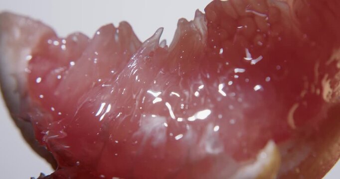 Fresh red grapefruit slice close up. Wet juicy surface background or texture. Slow rotation in changing local light.