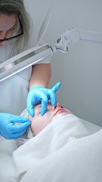 A skilled esthetician cosmetologist in blue gloves gently extracts blackheads using a metal tool during a classic deep pore cleansing session.