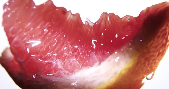 Fresh red grapefruit slice close up. Wet juicy surface background or texture. Slow rotation in changing local light.