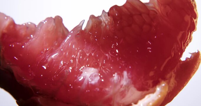 Fresh red grapefruit slice close up. Wet juicy surface background or texture. Slow rotation in changing local light.