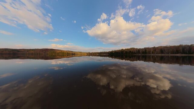 Dynamic sunrise timelapse of fast-moving lake ripples with vibrant autumn forest reflection, golden light shimmering on water surface