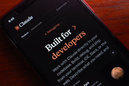 Quito, ECUADOR - Mar 9 2026 : Close-up of a smartphone displaying Claude Code&rsquo;s developer page on a wooden desk, highlighting AI coding tools and software development.