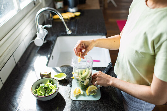 Woman preparing green smoothie in home kitchen