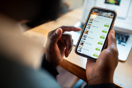 Customer ordering coffee on smartphone at cafe table