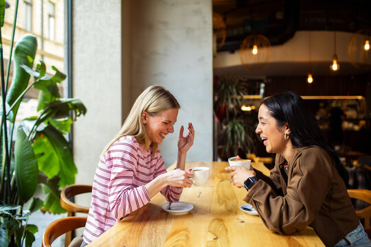 Two female friends laughing over coffee in a cozy cafe