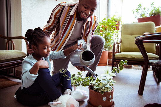 Father helping daughter water plants on balcony