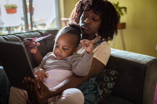Mother checking sick toddler's temperature during telehealth at home