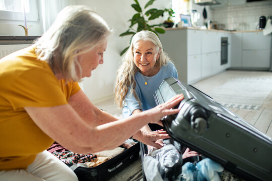 Two senior women packing a suitcase in home kitchen