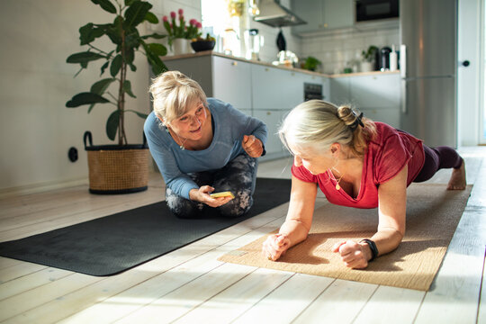 Two senior women doing plank exercise at home kitchen