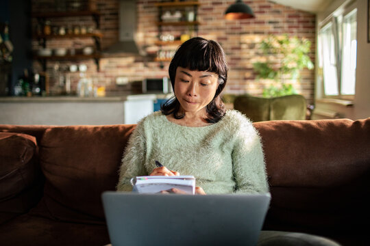 Woman taking notes while working on laptop at home