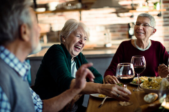 Senior friends laughing over dinner in cozy kitchen