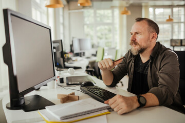 Fototapeta premium Focused mid adult man working at desktop computer in modern open plan office