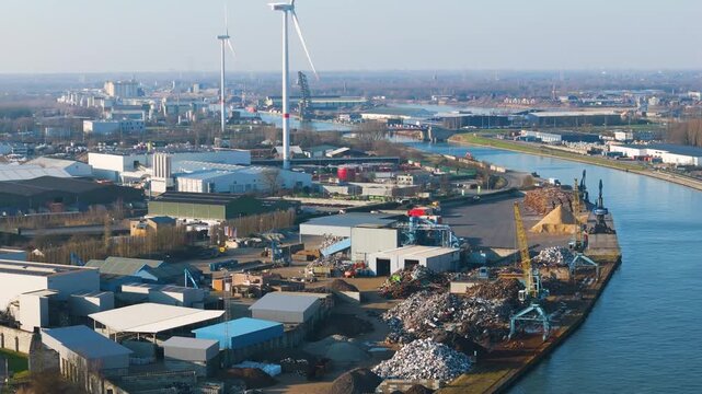 canal scrapyard towering mixed metal piles yellow blue cranes warehouses processing buildings wind turbines port complex willebroek near rising side canal-side 
