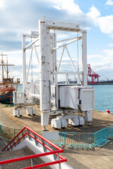 Fototapeta premium Large white mobile passenger gangway on wheels at a busy harbor. Professional boarding bridge for ships located on a dock under a bright sky with industrial port equipment in the background.