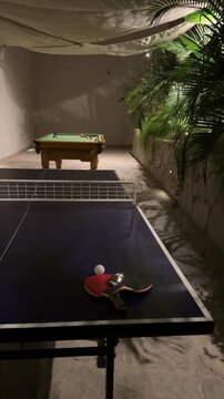 Luxury resort game zone at night with table tennis and billiard table. Cozy outdoor entertainment area with tropical plants and warm lighting in a high-end all-inclusive hotel patio.