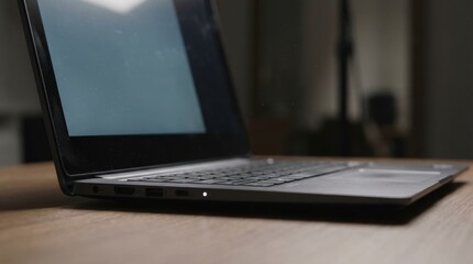 Fototapeta premium sleek black laptop sits open on wooden desk in dimly lit room