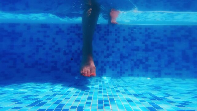 Underwater view of woman enter and walk in swimming pool with playful ripples