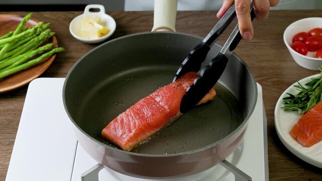 Cooking pan seared salmon moment, sliced salmon with rosemary in nonstick teflon coating pan with garlic, vegetables.
