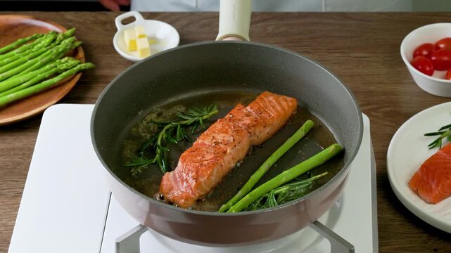 Cooking pan seared salmon moment, sliced salmon with rosemary in nonstick teflon coating pan with garlic, vegetables.
