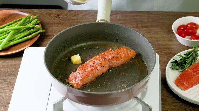Cooking pan seared salmon moment, sliced salmon with rosemary in nonstick teflon coating pan with garlic, vegetables.