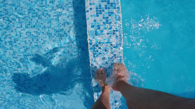 Bare leg person steps and walk onto submerged stairs in a swimming pool with vibrant blue water surrounded by sunlight reflections