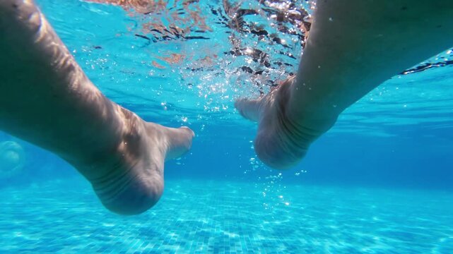 Underwater view of moving swinging legs in a clear swimming pool