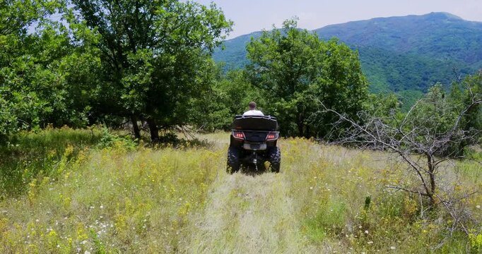 Unrecognizable rescuer man riding atv quad vehicle through scenic mountain forest landscape