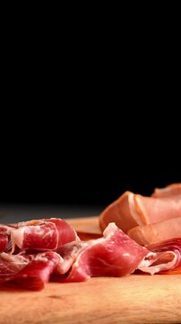 Close-up of thin cold cut meat slices on a rustic wooden surface, charcuterie board