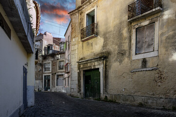 Obraz premium A narrow cobblestone alley with abandoned residential buildings in the medieval hillside Alfama district of Lisbon, Portugal.
