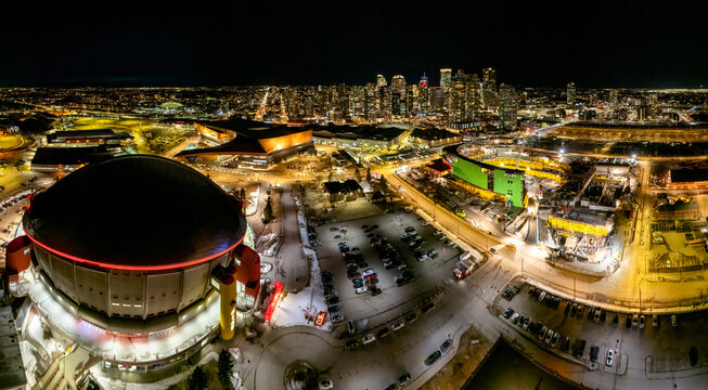 Calgary, Alberta, Canada. March 13, 2026. Panoramic night aerial view of the Scotiabank Saddledome, BMO Centre, and downtown Calgary skyline.