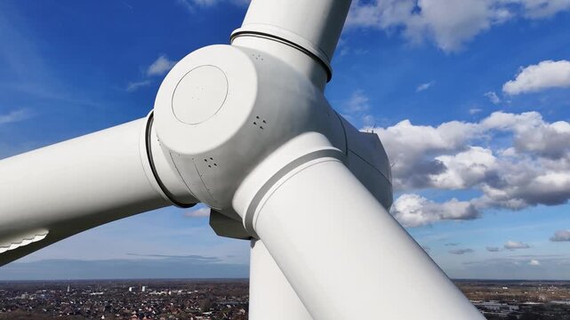 wind turbine nacelle blades tower above sprawling town renewable energy technology urban landscapes under clear sky scattered clouds integration sustainable power infrastructure 