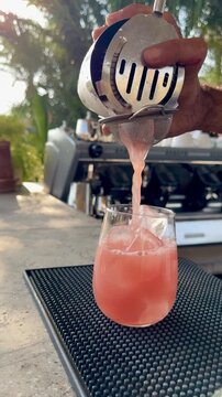 Professional bartender pouring pink cocktail through a strainer into a glass with ice. Crafting a refreshing summer drink at a luxury Arabian all-inclusive resort bar in Hurghada, Red Sea, Egypt.