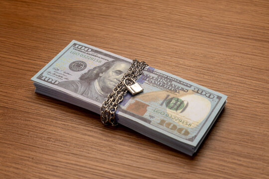 A bundle of one hundred US dollar bills bound with a metal chain and secured with a padlock. Financial security, asset protection, frozen accounts, and investment safety concept.