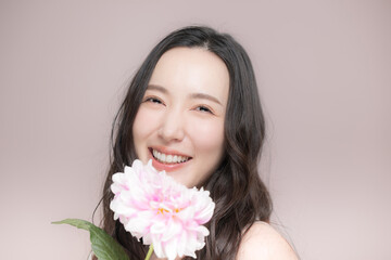 Fototapeta premium ダリアの花を持って多幸感にあふれるピンクの春色イメージの女性の美容ビューティーイメージカメラ目線 ピンク背景