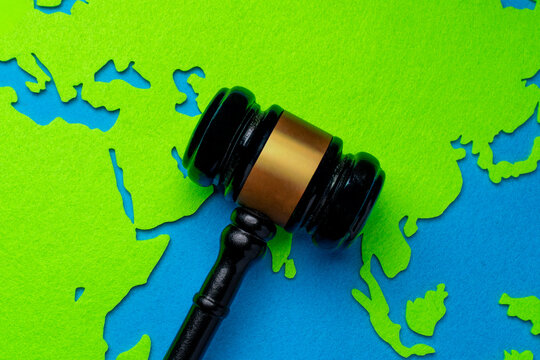 Top down view of a judge's gavel on a paper world map cutout. International law, global justice, environmental regulations, human rights, and cross-border legal jurisdiction concept.