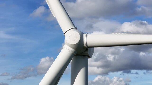 wind turbine central hub thick rotor blades tilt against bright blue sky layered clouds engineering strength environmental benefits sustainable electricity rural area energy technology 