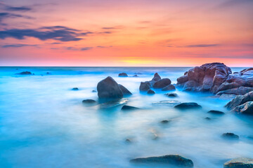 Obraz premium Beautiful coastal sunrise scene featuring a dramatic rock formation rising from a sandy beach.