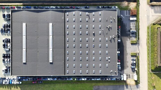 perspective large industrial warehouse twin roof sections skylight strips vents tightly arranged parking rows narrow canal running parallel to overhead aerial packed 