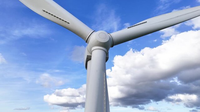low wind turbine hub three blades against bright blue sky drifting cumulus clouds white surfaces aerodynamic contours renewable smooth angle view energy 
