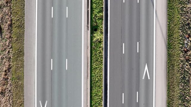 vertical perspective two cars moving along separate carriageways divided highway split by narrow grassy median crisp white lane markings large directional arrow drone belgium 