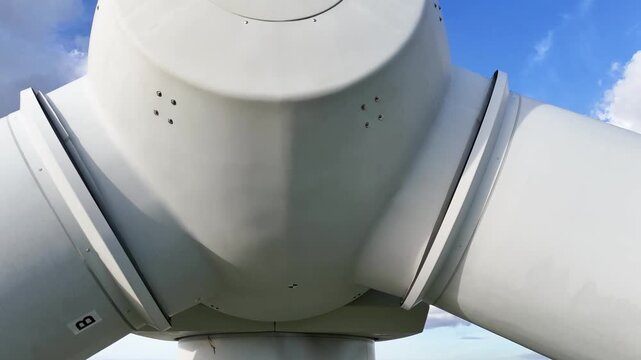 extreme wind turbine rounded hub connecting thick white blades set below bright blue sky scattered clouds engineering structure reveals up close precision structural detail 
