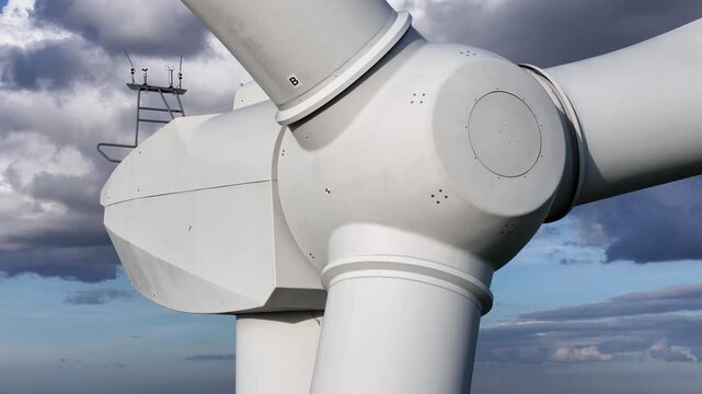 wind turbine central hub thick blades surfaces bolts framed by overcast sky sustainable electricity generation up close smooth structure close-up precision mechanical details 