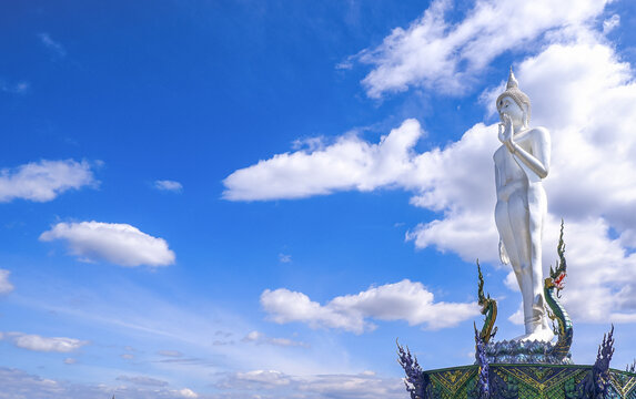 Majestic white standing Buddha statue at Wat Khao Phra Khru in Chon Buri, Thailand, set against a bright blue sky.