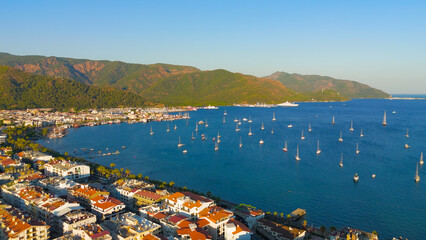 Marmaris, Turkey. Luxury yachts and sailboats anchored in Marmaris Bay during spectacular sunset. Warm golden sunlight illuminates the calm water and forested mountains.. Aerial View © Video Render